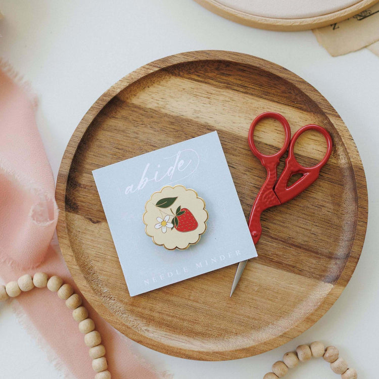 Strawberry magnetic needle minder holding a needle on an embroidery hoop