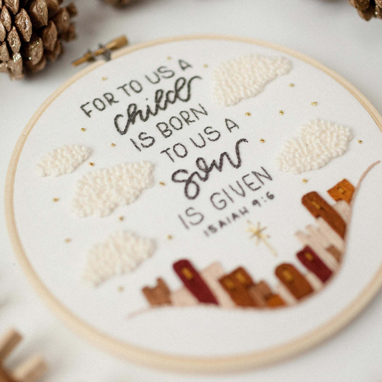 Close-up of the For to Us a Child Is Born Advent embroidery — Isaiah 9:6 with the Bethlehem skyline and French-knot clouds