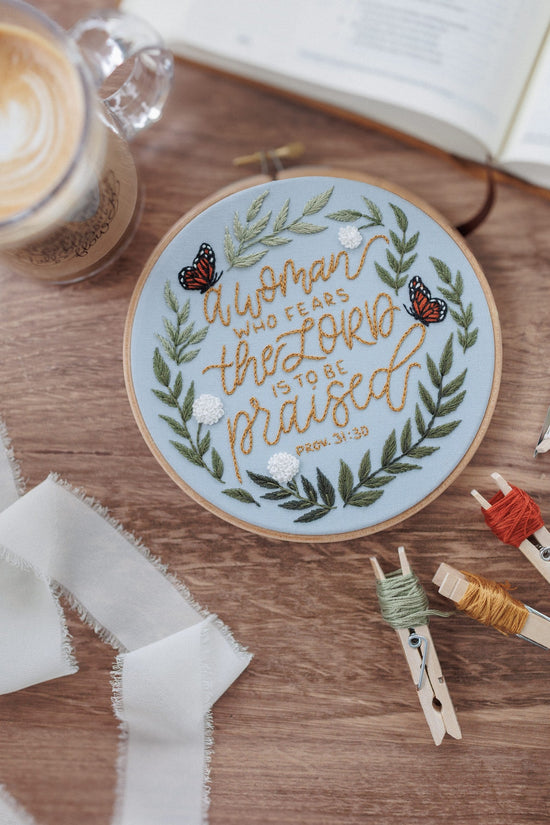 Finished Proverbs 31 hoop on a walnut table with floss and scissors