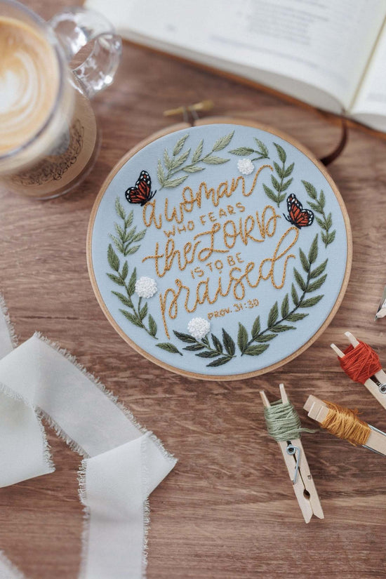 Finished Proverbs 31 hoop on a walnut table with floss and scissors