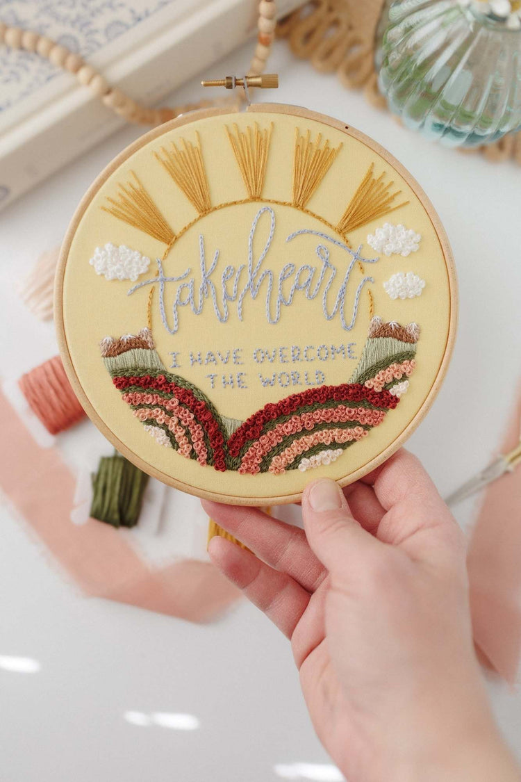 Hand holding the finished Take Heart John 16:33 hoop to show scale