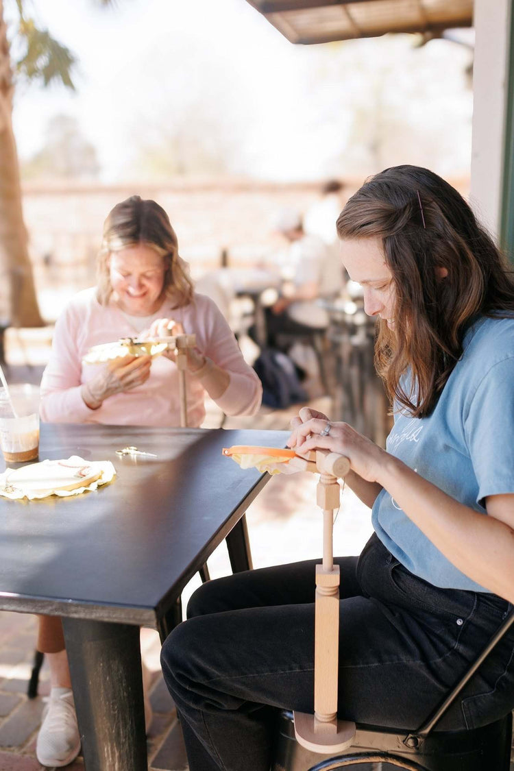 Two stitchers using embroidery hoop stands side by side at an outdoor table