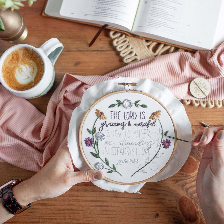 The Lord Is Gracious and Merciful embroidery kit on a wood table with coffee