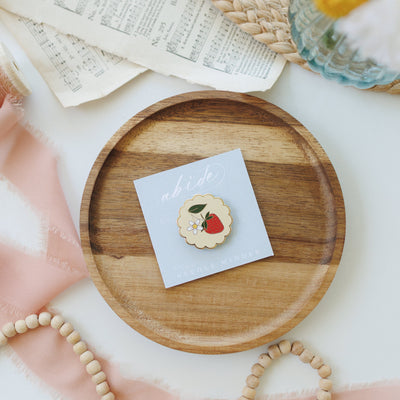 Strawberry enamel needle minder — magnetic embroidery needle minder on a peach scalloped background edged in gold