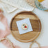 Strawberry enamel needle minder — magnetic embroidery needle minder on a peach scalloped background edged in gold