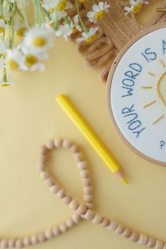 Your Word Is a Lamp kids embroidery hoop styled with daisies, a yellow pencil and wooden beads | Abide Kids