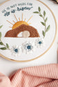 Close-up of the He Is Risen empty-tomb embroidery — stitched sunrise, tomb and anemone flowers