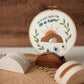 He Is Risen Easter embroidery hoop displayed on a walnut stand against warm wood