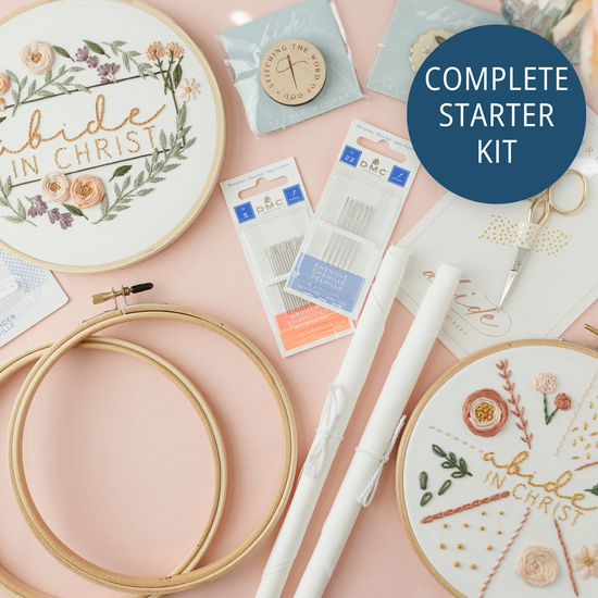 Complete Embroidery Starter Kit flat lay with the Abide in Christ and 17-stitch practice hoops, gold scissors, needle minders, extra hoops, fabric and DMC needles