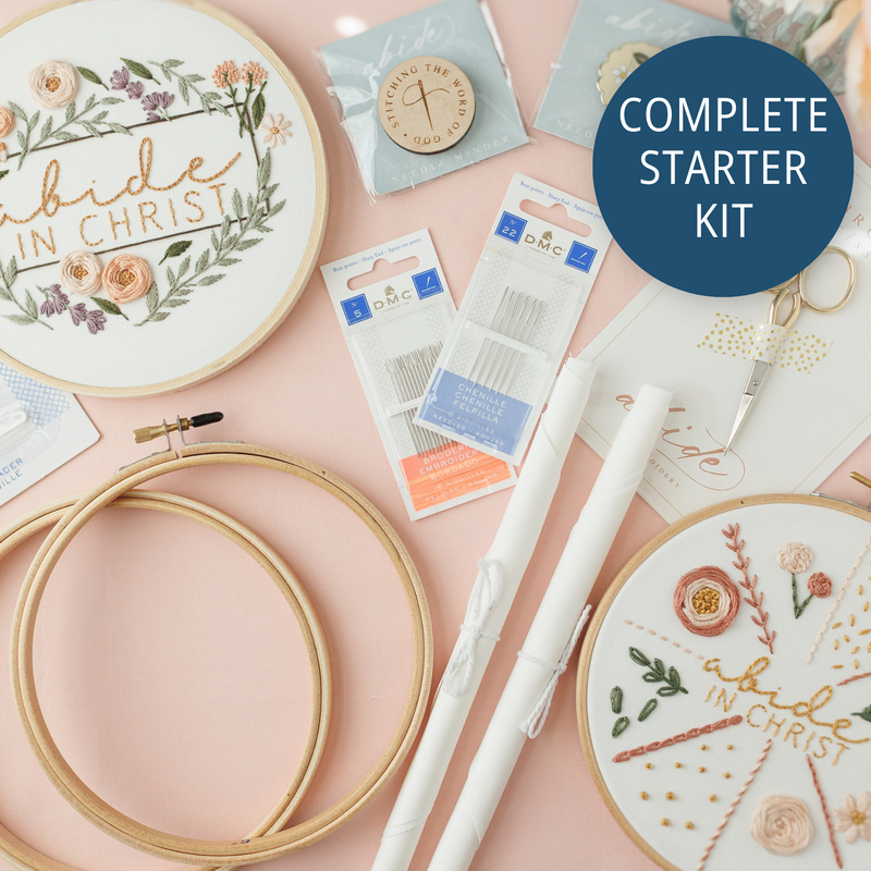 Complete Embroidery Starter Kit flat lay with the Abide in Christ and 17-stitch practice hoops, gold scissors, needle minders, extra hoops, fabric and DMC needles