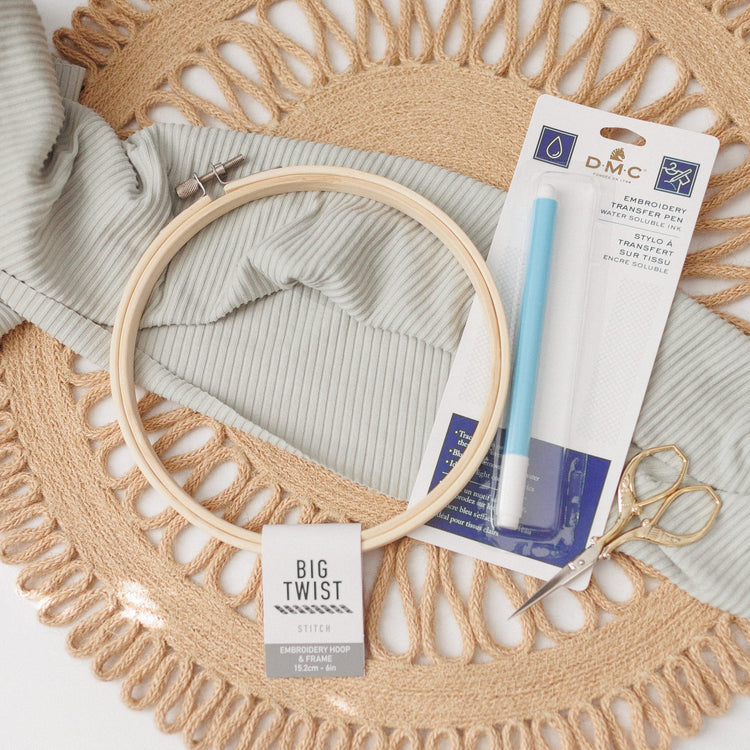 DMC embroidery transfer pen in packaging with a wooden hoop, fabric and gold scissors