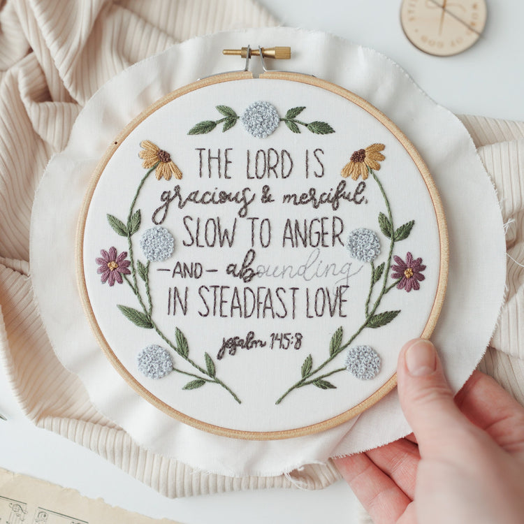 Hand holding the finished Psalm 145:8 embroidery hoop to show scale