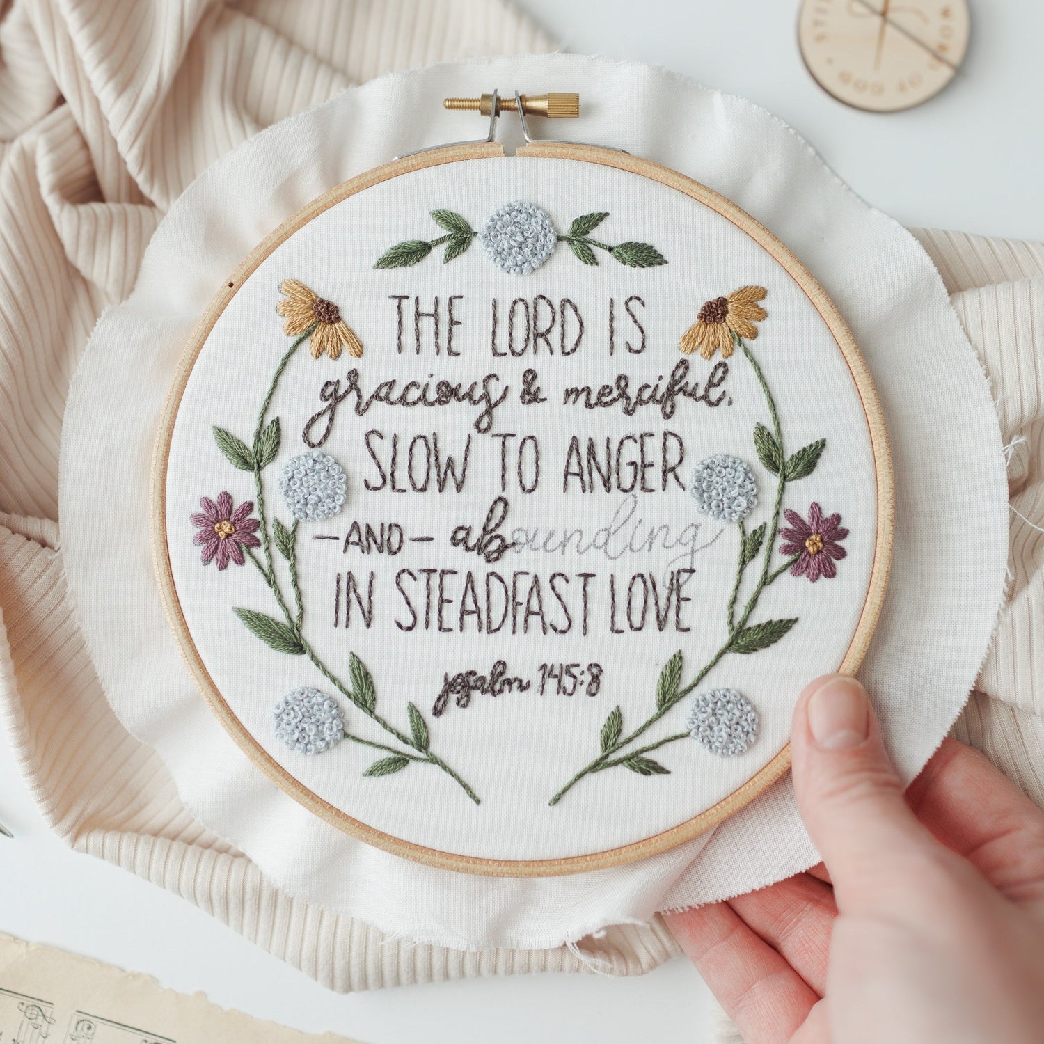 Hand holding the Psalm 145:8 embroidery hoop to show scale