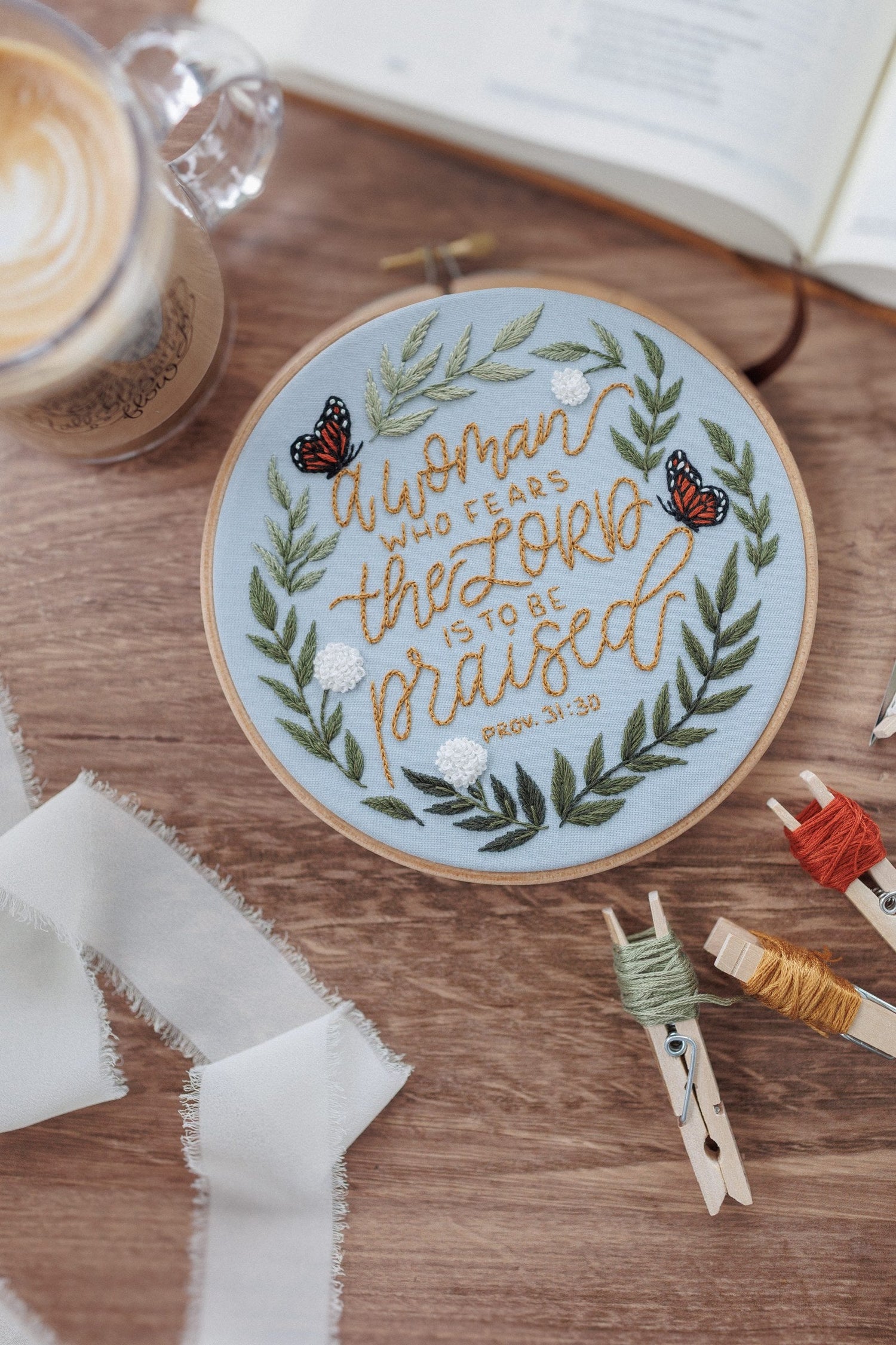 Finished Proverbs 31 hoop on a walnut table with floss and scissors