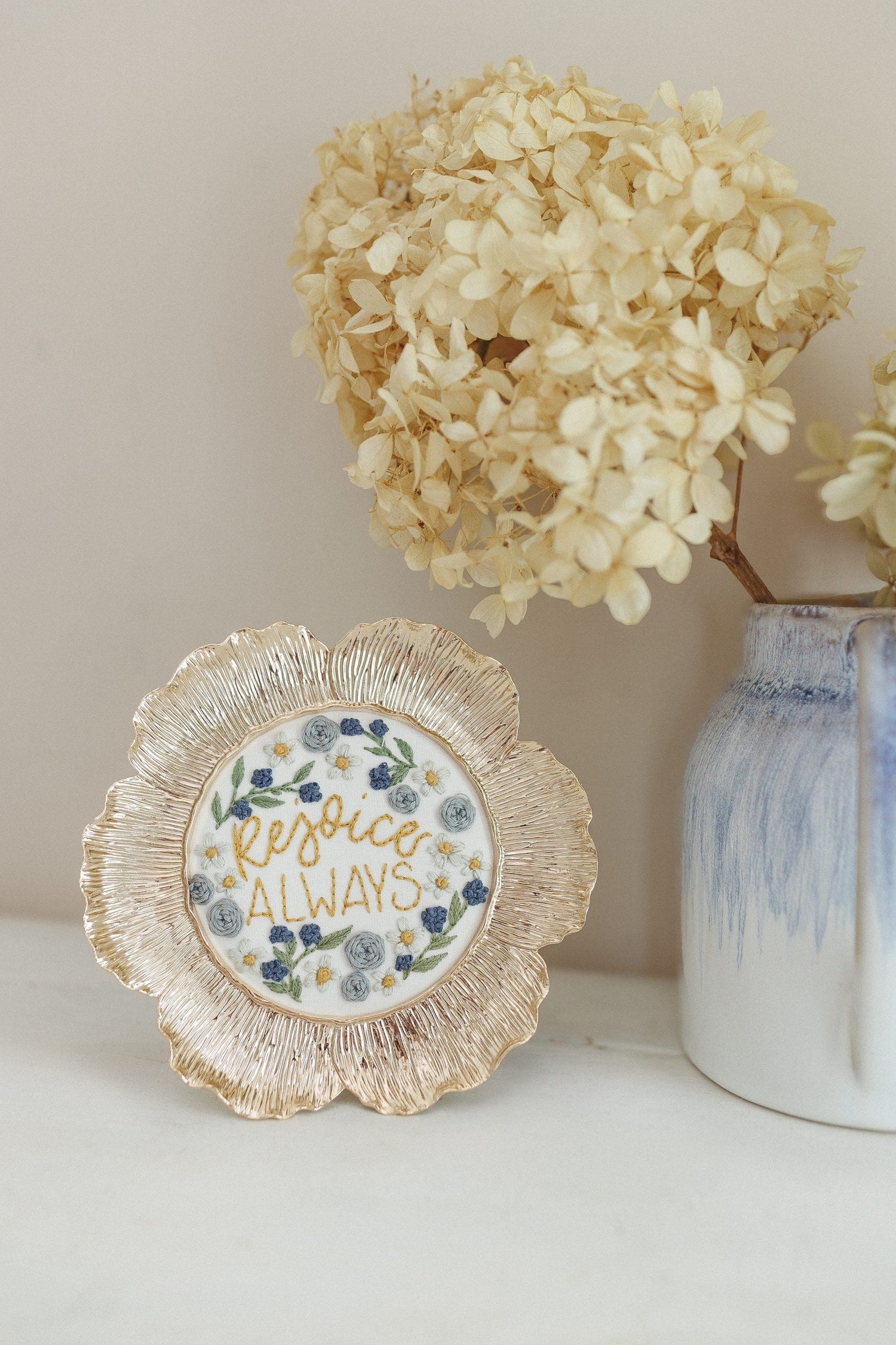 Finished Rejoice Always piece beside a vase of dried hydrangea