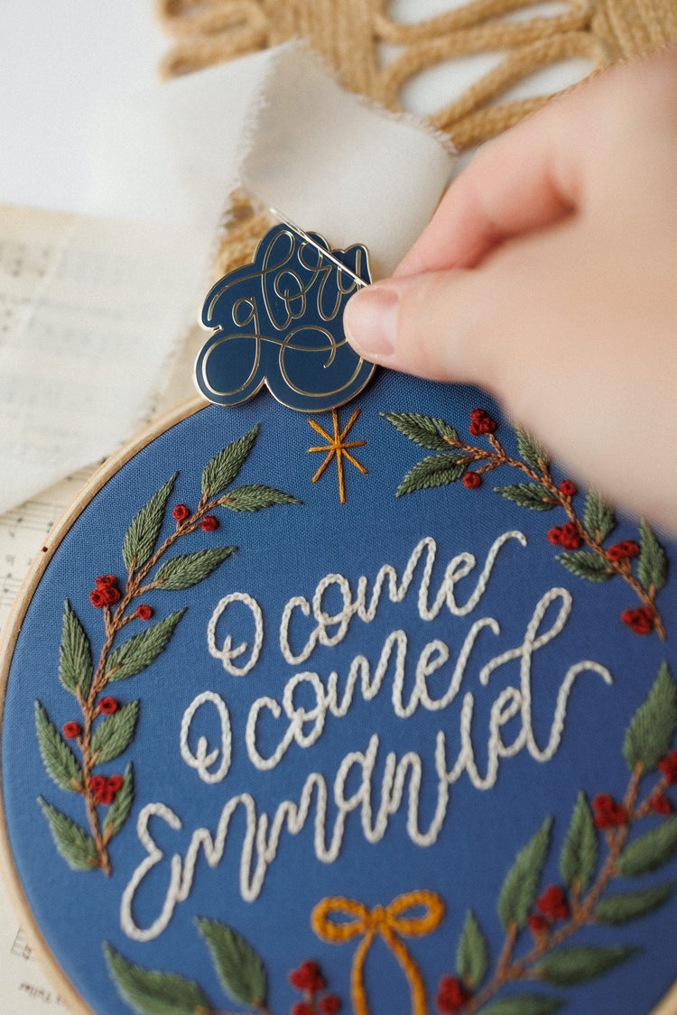 Close-up detail — hand placing the Glory ornament beside the finished hoop