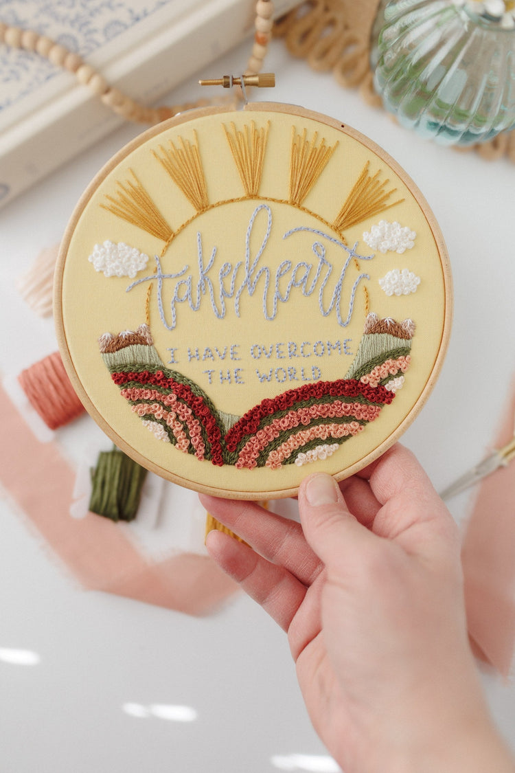 Hand holding the finished Take Heart John 16:33 hoop to show scale