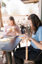 Two stitchers using embroidery hoop stands side by side at an outdoor table