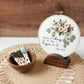 Job 13:15 embroidery hoop displayed on a walnut stand with floss in a wooden bowl